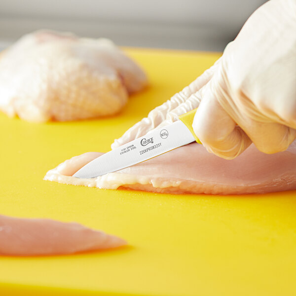 A person using a Choice 3 1/4" Smooth Edge Paring Knife with a yellow handle to cut chicken.