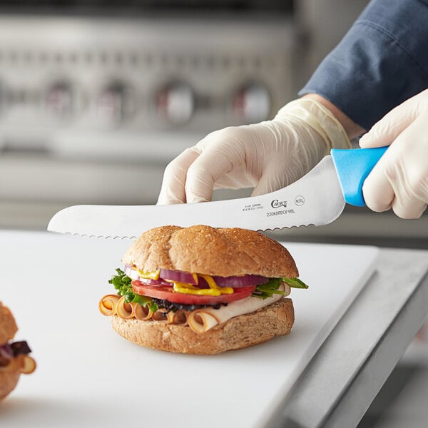 A person in a white coat using a Choice offset serrated bread knife with a blue handle to cut a sandwich.
