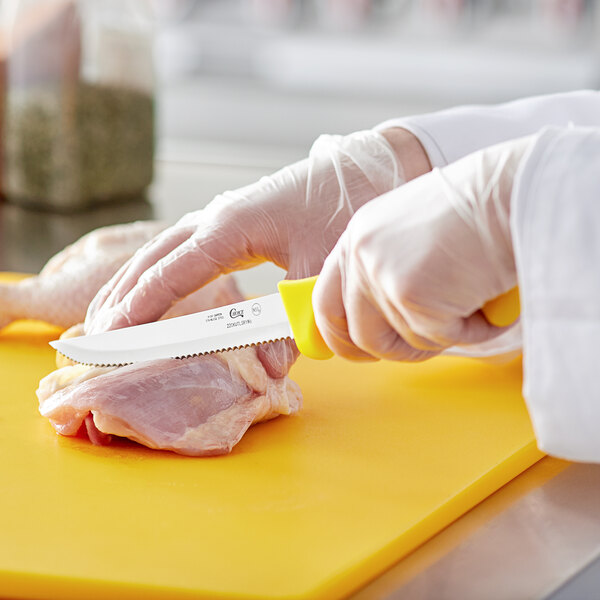 A person in white gloves using a Choice 6" serrated utility knife with a yellow handle to cut meat.