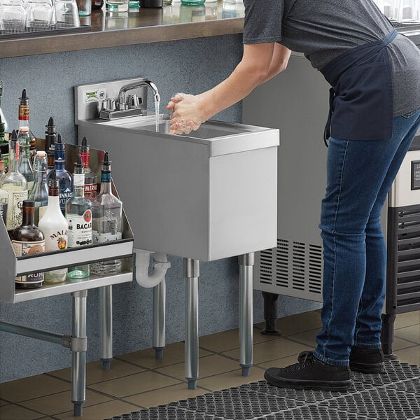 A woman washing her hands at an underbar sink.