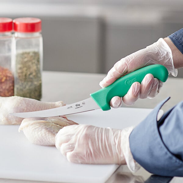 A person in a white coat using a Choice curved stiff boning knife with a green handle to cut chicken.