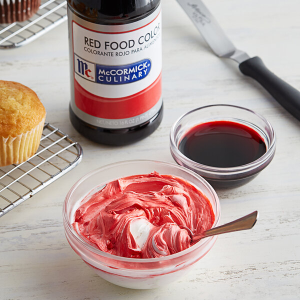A cupcake with red frosting next to a bottle of McCormick red food coloring.