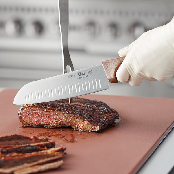 A person using a Choice Santoku knife to cut a steak on a cutting board.