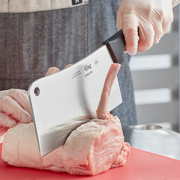 A person using a Choice stainless steel cleaver to cut meat on a cutting board.