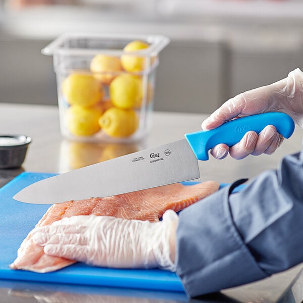 A person using a Choice 10" Chef Knife to cut a piece of meat.
