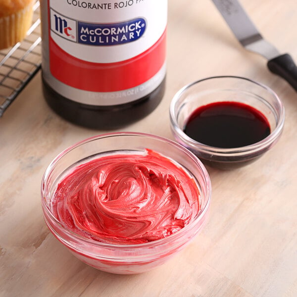 A bowl of red frosting next to a bottle of McCormick Culinary Red Food Color.