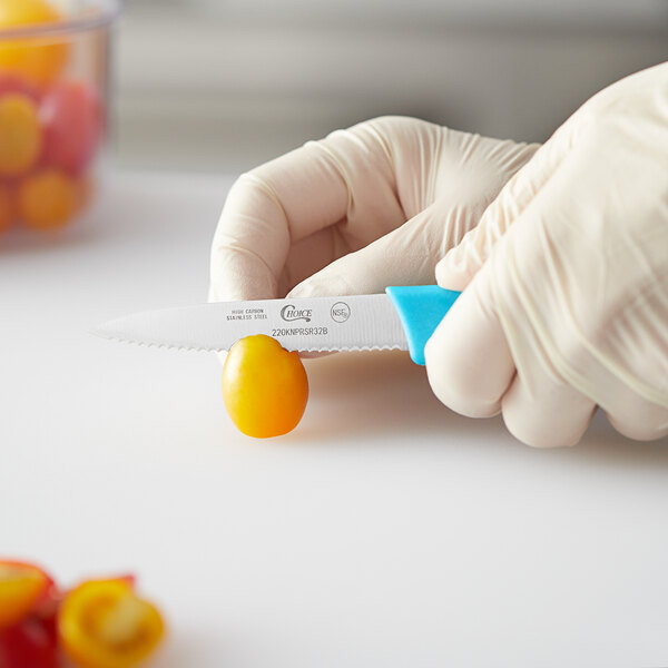 A person in gloves uses a Choice serrated paring knife with a neon blue handle to cut a tomato.