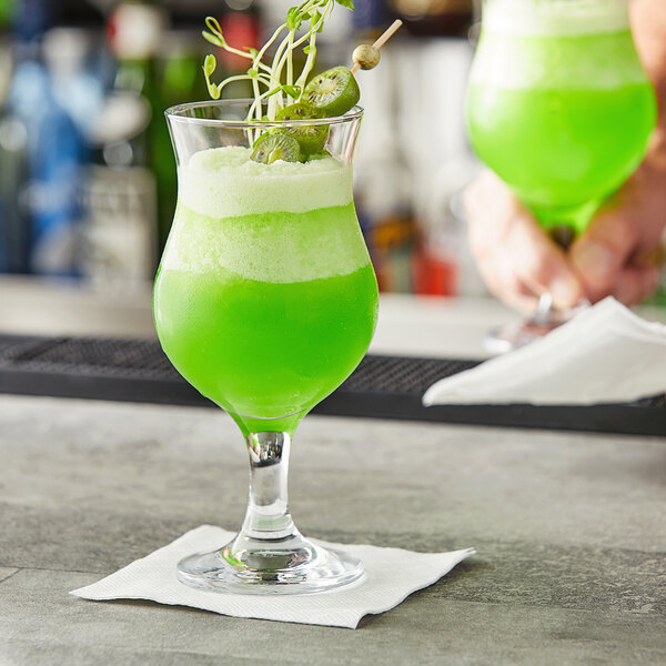 A hand holding a green drink in a Pasabahce Capri Poco glass.