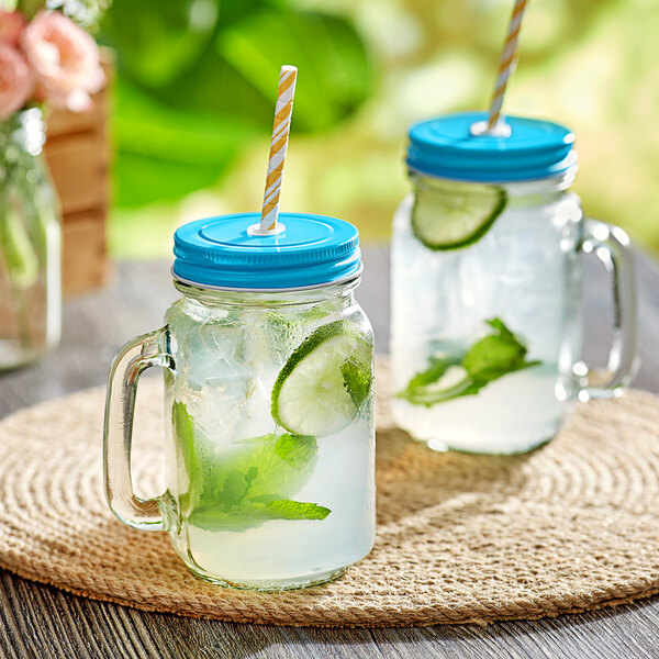 Two Acopa glass jars with light blue lids and straws filled with drinks.