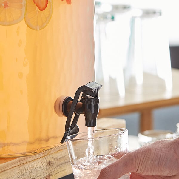 A hand pouring water from an Acopa black spigot into a glass.