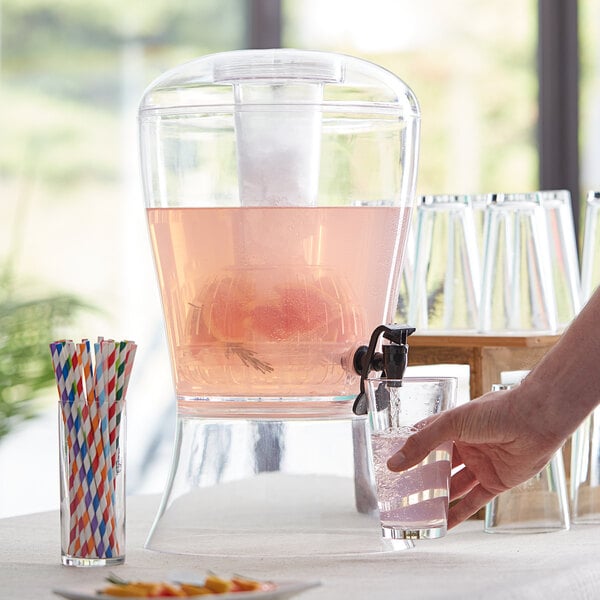 A person pouring pink liquid into a Choice acrylic beverage dispenser with colorful straws.