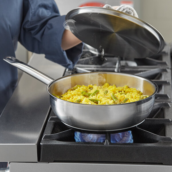 A person cooking food in a Vigor stainless steel saucier pan on a stove.
