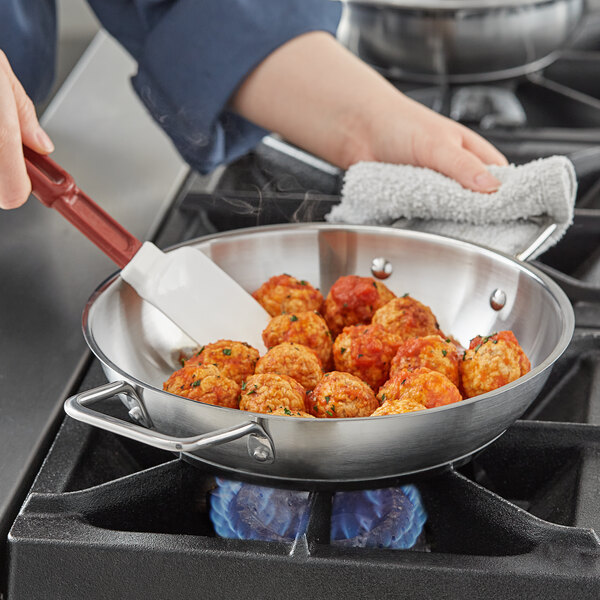 A person cooking meatballs in a Vigor stainless steel fry pan with dual handles.
