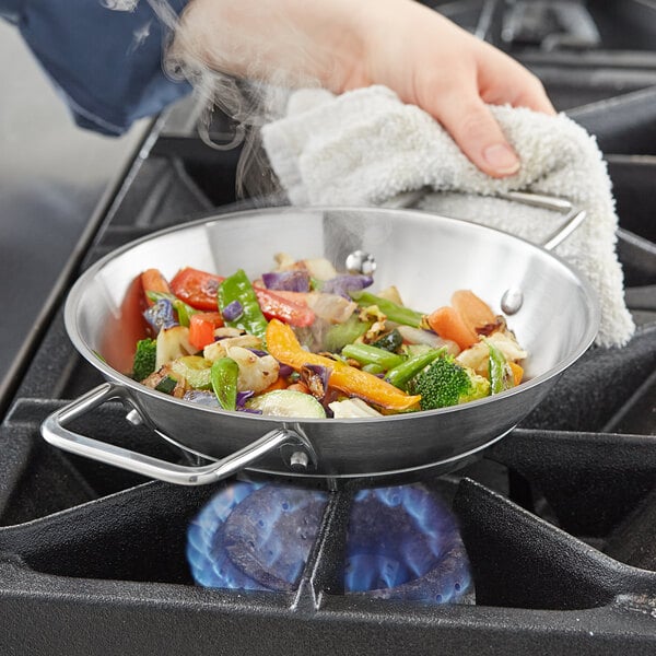 A person cooking vegetables in a Vigor stainless steel fry pan on a stove.