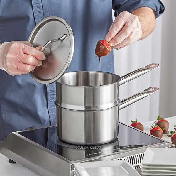A person using a Vigor stainless steel double boiler to pour chocolate over strawberries on a stove.