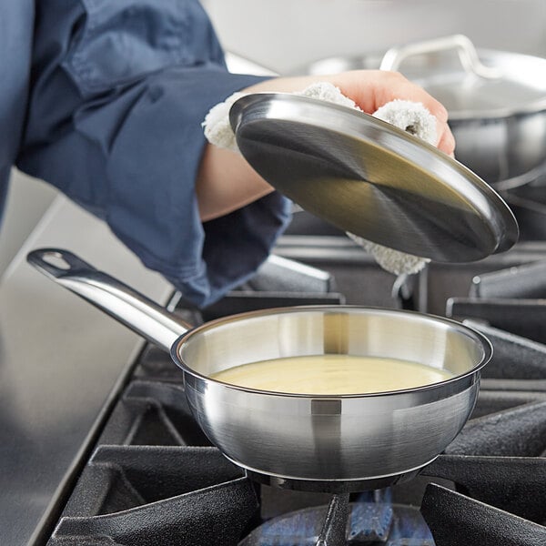 A person cooking with a Vigor stainless steel saucier pan on a stove.