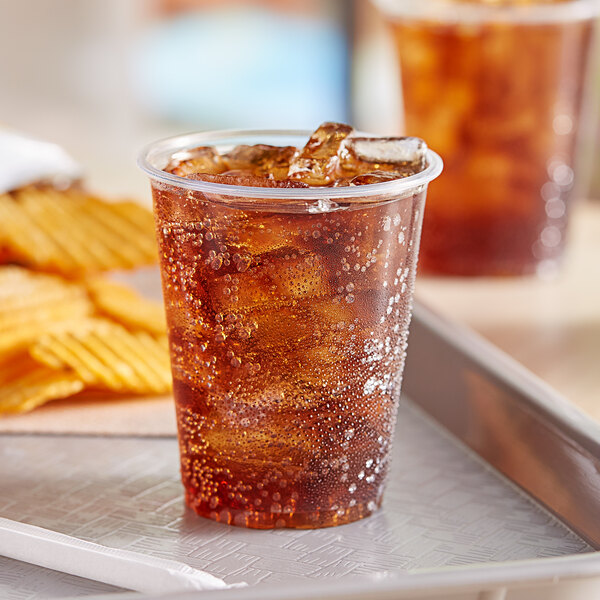 A plastic EcoChoice PLA cold cup with a brown drink in it on a tray of chips.