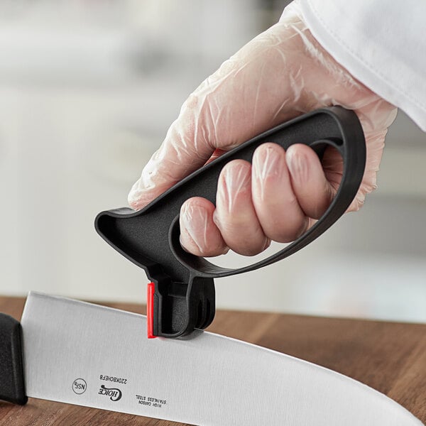 A hand in a clear glove sharpening a black-handled knife.