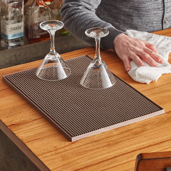 A man wiping wine glasses on a wood bar mat.