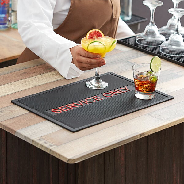 A person using a Choice Black and Red Service Bar Mat to serve a drink on a bar counter.