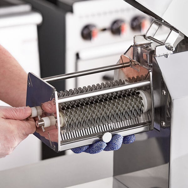 A person using an Avantco meat tenderizer blade set to cut up a piece of meat.