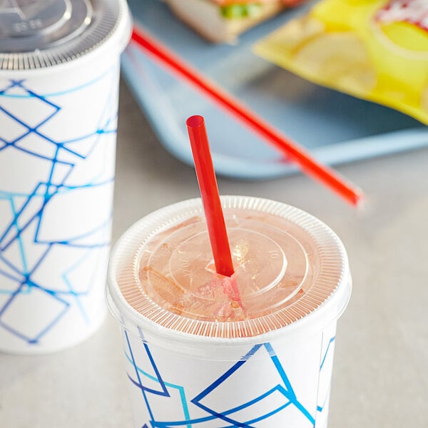A plastic cup with a red straw in it on a plate with another cup and a sandwich.