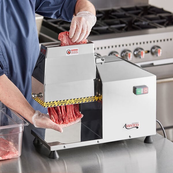 A person using an Avantco meat tenderizer on a counter.