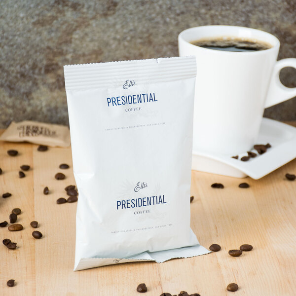 A white Ellis bag with blue text next to a cup of coffee.