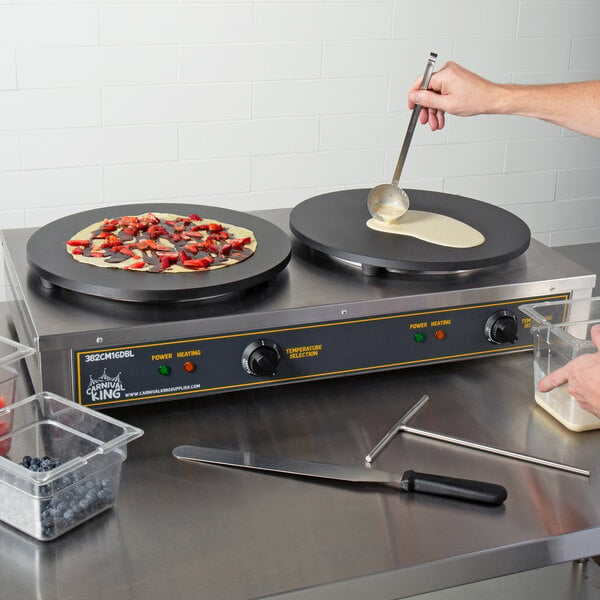 A person using a Carnival King Dual Non-Stick Crepe Maker to make food on a pan.