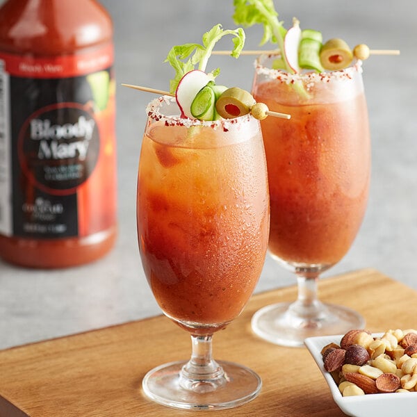 Two glasses of Regal Cocktail Bloody Mary mix with vegetables and nuts on a table.