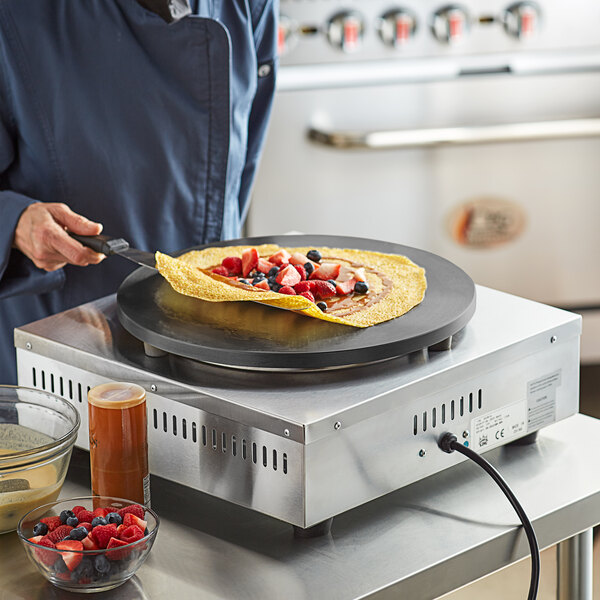 A person using a Carnival King crepe maker to cook a crepe with fruit.
