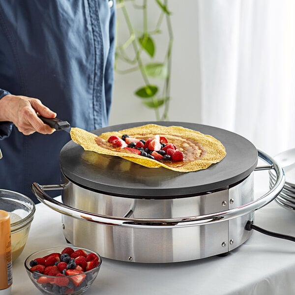 A person cooking a crepe on a Carnival King round portable crepe maker.