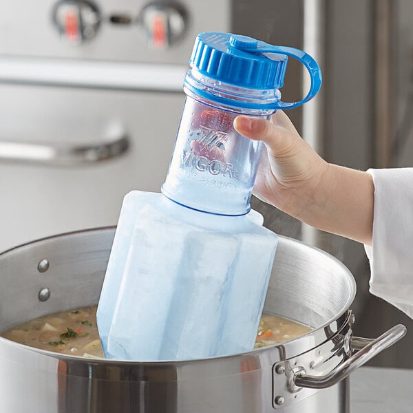 A hand holding a blue Vigor Polar Paddle bottle of liquid over a pot of soup.