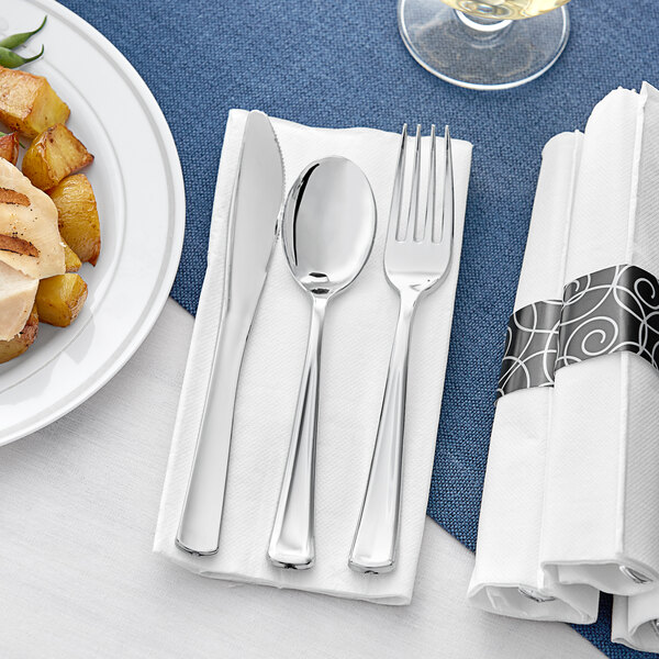 A white napkin with a pre-rolled metallic silver fork, knife, and spoon.