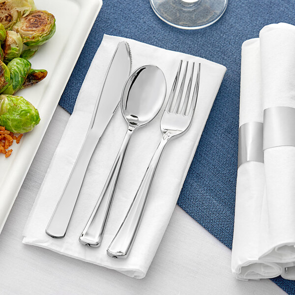 A white napkin with metallic silver plastic cutlery including a fork and knife.