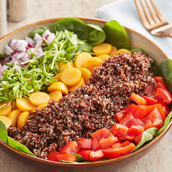 A bowl of salad with vegetables and red quinoa on a table.