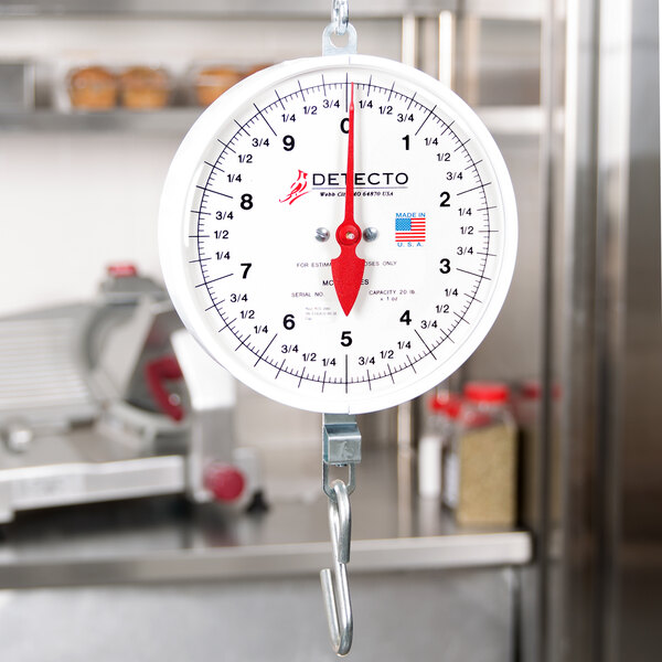 A Cardinal Detecto hanging hook scale with a white dial and a red handle.