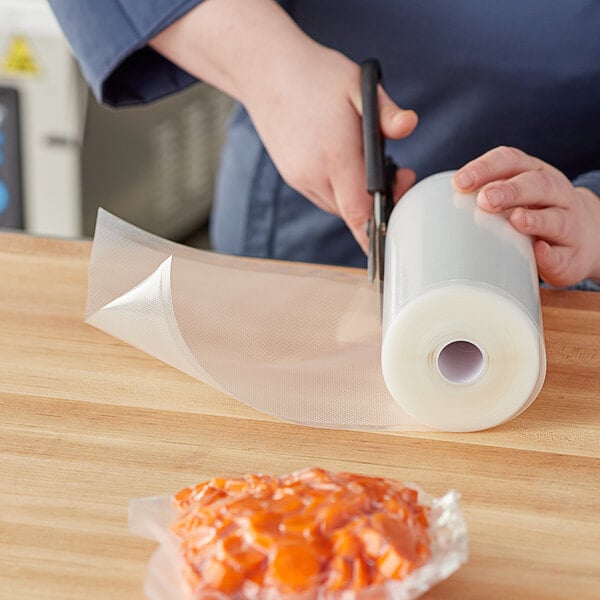 A hand cutting a roll of Choice Full Mesh External Vacuum Packaging Bags with scissors.