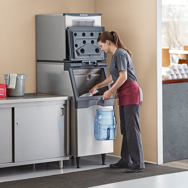 A woman in a red apron standing in front of a Scotsman air cooled nugget ice machine in a professional kitchen.