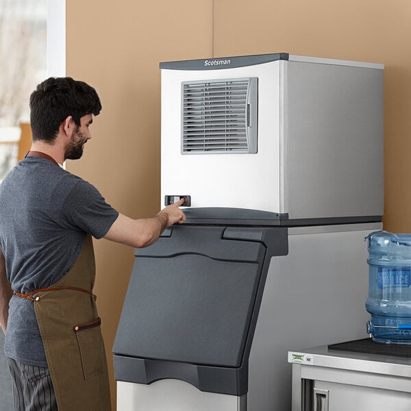 A man in a brown apron pushing a Scotsman air cooled nugget ice machine.