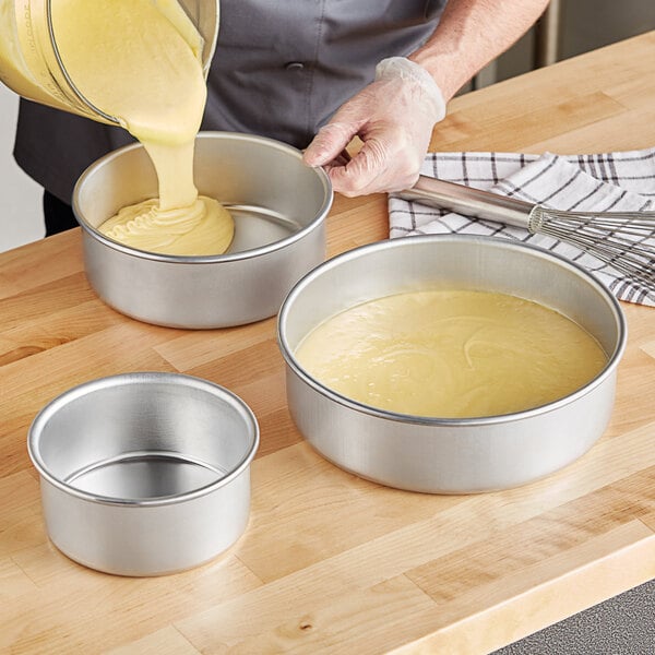 A person pouring yellow cake batter into a Choice round cake pan.