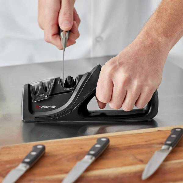 A person using a Wusthof handheld knife sharpener to sharpen a knife.