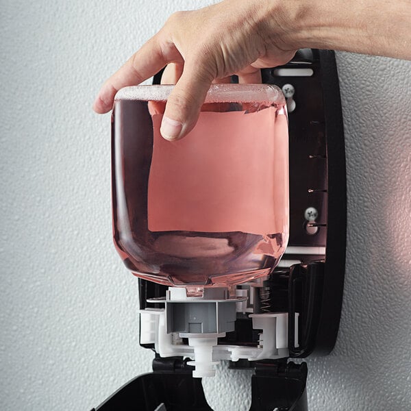 A hand holding a GOJO cranberry pink liquid soap dispenser.