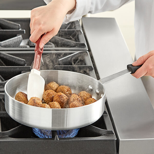 A person cooking meatballs in a Choice aluminum saute pan.