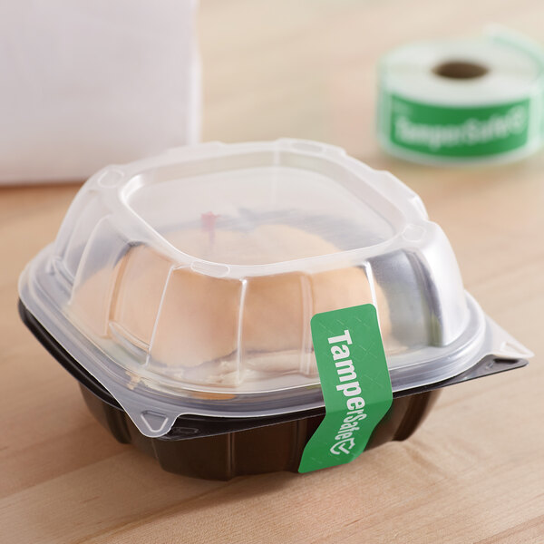 A plastic container with a clear lid and a roll of green TamperSafe labels.