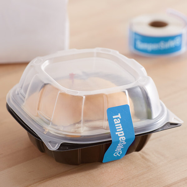 A plastic container with a clear lid labeled with a roll of blue TamperSafe stickers.