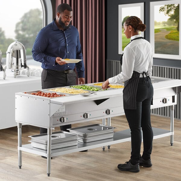 A man and woman standing next to a ServIt electric steam table on a hotel buffet table.