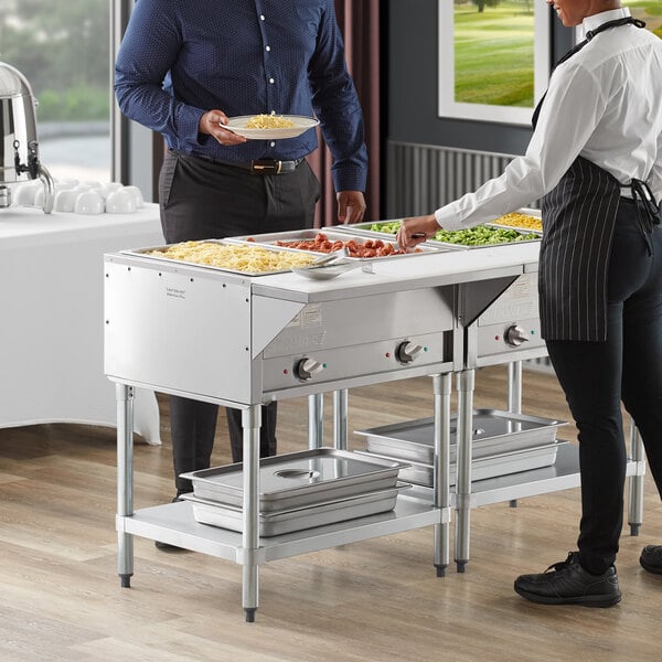 A man and woman serving food from a ServIt electric steam table at a buffet.