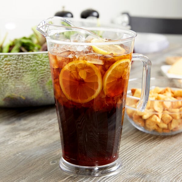 A Fineline clear plastic pitcher filled with ice tea and lemon slices on a white background.