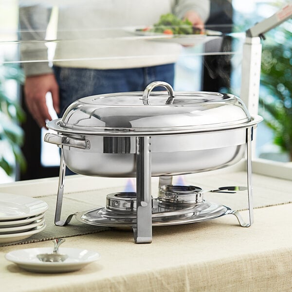 A stainless steel Choice Deluxe oval chafer with chrome accents on a table set with plates and silverware.